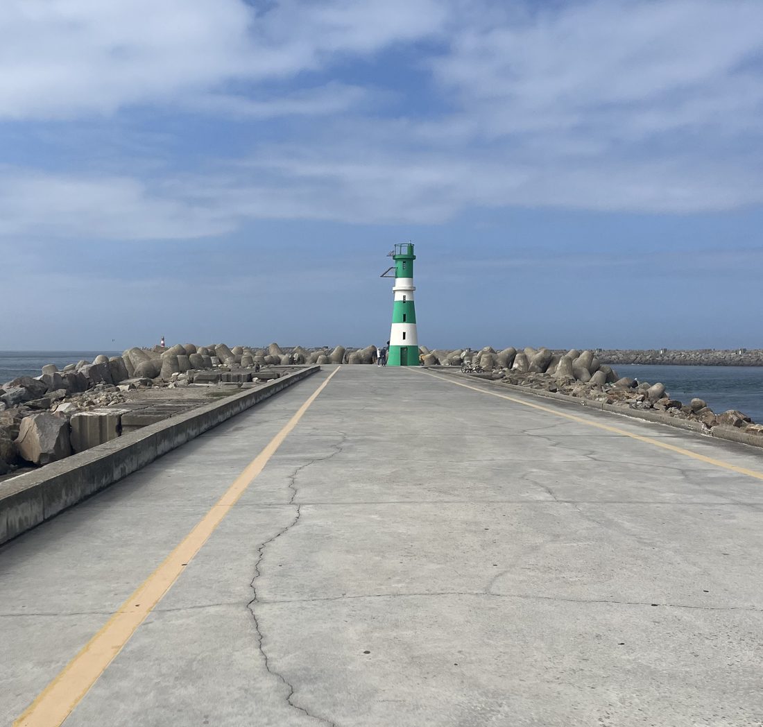 A green and white lighthouse at the end of a long pier